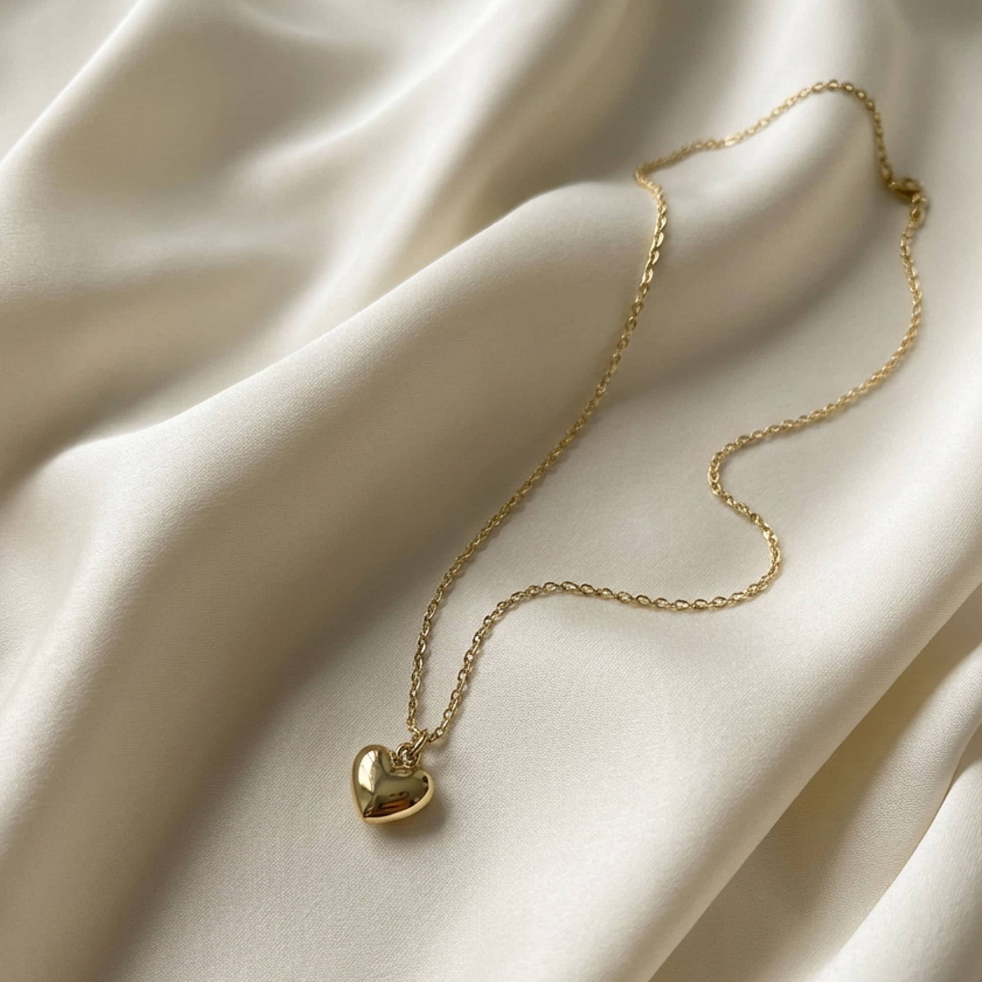 Złoty naszyjnik z zawieszką serce na delikatnym łańcuszku ułożony na jedwabnej tkaninie