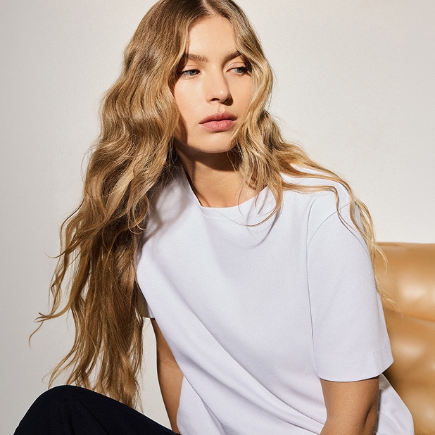 Kobieta w prostej białej koszulce i naturalnym makijażu na neutralnym tle